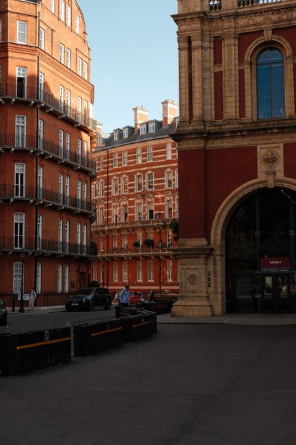 A view of a historic building entrance in Marylebone, featuring a large arched stone doorway with an ornate black iron gate that has decorative patterns and a central lock. The building's facade is ma